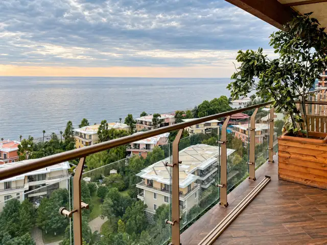 Sea view from a glass-railed balcony at golden hour with potted greenery