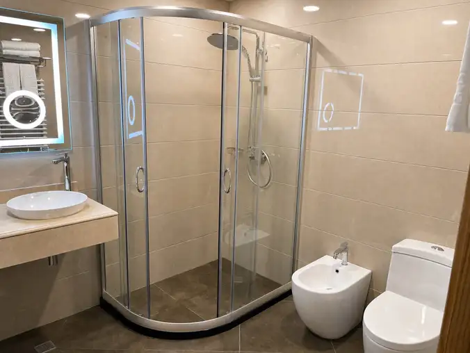 Studio Sea View & Mountain — Walk-in glass shower with bidet and toilet in the beige-tiled bathroom