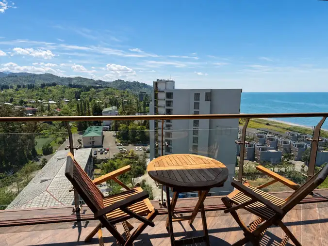One Bedroom Sea View & Mountain — Balcony table and chairs overlooking the sea, mountains and town on a sunny day One Bedroom Sea View & Mountain — Balcony table and chairs overlooking the sea, mountains and town on a sunny day