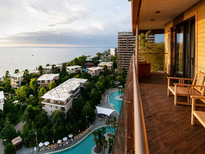One Bedroom Sea Front & Pool View — Wide balcony at golden hour with bench and pool & sea panorama