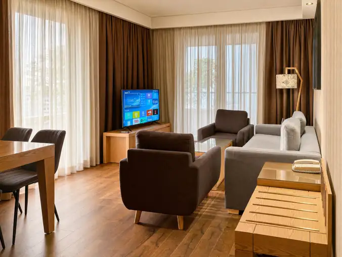 One Bedroom Sea Front & Pool View — Living room with sofa, armchairs, mounted TV and dining area