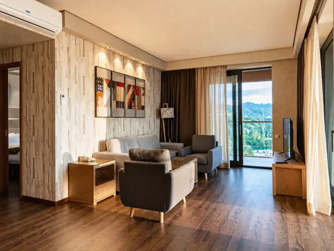 One Bedroom Sea Front & Batumi Side — Open lounge with sofa, armchair, bedroom doorway and balcony access