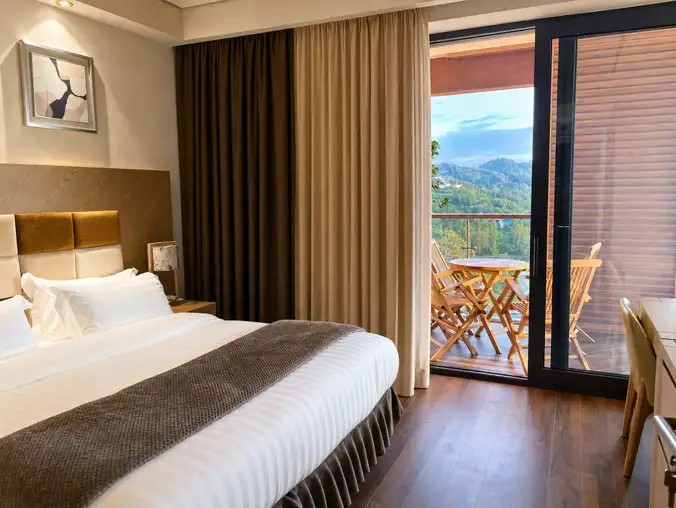 One Bedroom Sea Front & Batumi Side — King bed with balcony access showing wooden chairs and mountain view
