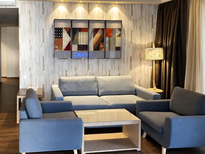 One Bedroom Sea Front & Batumi Side — Lounge with grey sofa, blue armchairs and large abstract artwork
